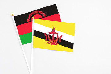 Brunei and Malawi stick flags on white background. High quality fabric, miniature national flag. Peaceful global concept.White floor for copy space.