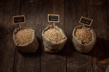 Grain of wheat, rye and barley in small burlap sacks on a wooden table. Name of the variety of grains on a wooden plate frame. Rustic, farm concept. Copy space. Top view