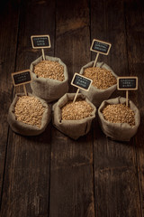 Grain of wheat, rye and barley in small burlap sacks on a wooden table. Name of the variety of grains on a wooden plate frame. Rustic, farm concept. Copy space