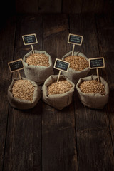 Grain of wheat, rye and barley in small burlap sacks on a wooden table. Name of the variety of grains on a wooden plate frame. Rustic, farm concept. Copy space