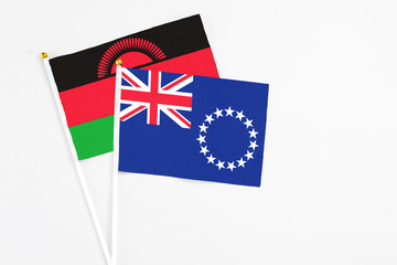 Fototapeta premium Cook Islands and Malawi stick flags on white background. High quality fabric, miniature national flag. Peaceful global concept.White floor for copy space.