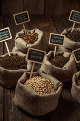 Grain of wheat, rye and barley in small burlap sacks on a wooden table. Name of the variety of grains on a wooden plate frame. Rustic, farm concept. Copy space