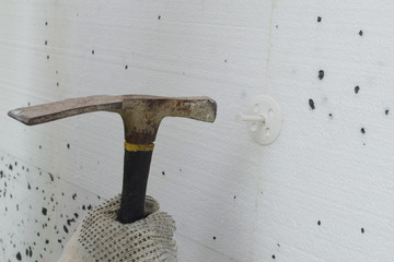 Constraction worker gloved hand using hammer to hammer white plastic screw anchor dowel with bolt...