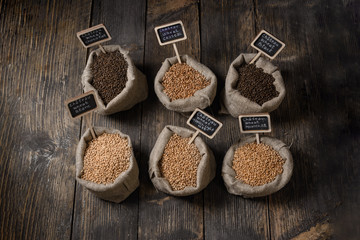 Grain of wheat, rye and barley in small burlap sacks on a wooden table. Name of the variety of grains on a wooden plate frame. Rustic, farm concept. Copy space. Top view