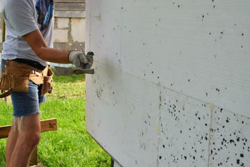 Constraction worker gloved hand using hammer to hammer white plastic screw anchor dowel with bolt and round hat into polystyrene foam plates for building wall insulation. House improvement and DIY con