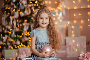 Fototapeta na wymiar cheerful beautiful Girl in an elegant dress holds a Christmas-tree decoration in her hands. she is waiting for the New Year holiday, behind her is a Christmas tree in the lights