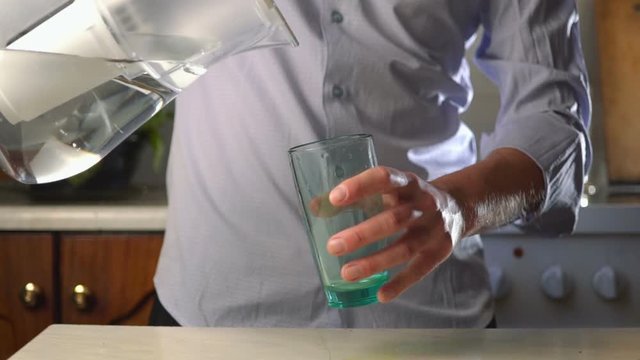 man pours purified water into a glass from a pitcher with a filter. filtered drinking water
