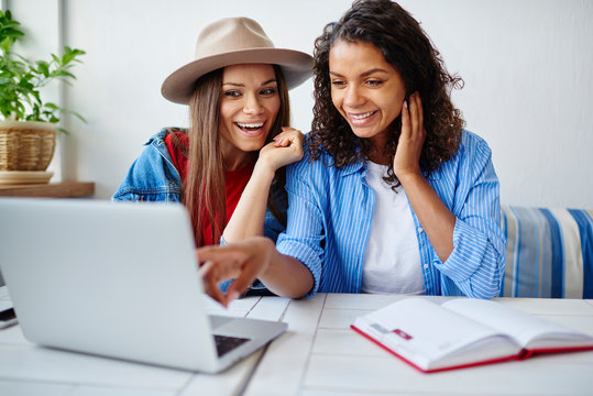 Cheerful african american woman pointing on netbook showing funny pictures from social networks to her best friend,smiling multiracial hipster girls watching movie on laptop computer during leisure