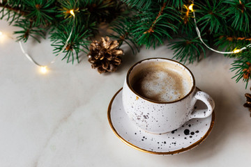 Christmas composition with cup of coffee surrounded by fir brunches with golden bumps and on marble background. with copy space