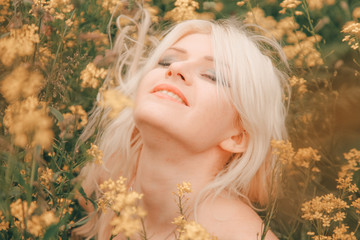 beautiful young blonde woman on the meadow with yellow flowers on a warm summer day