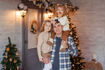 Young father with two daughters having fun outdoors in the snow against the background of a wooden house with a veranda awaiting Christmas.