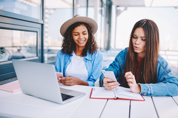 Positive female bloggers sharing media files via bluetooth connection on smartphone devices while...