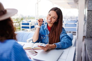 Pretty caucasian female laughing during conversation with friend checking mail on telephone,cheerful hipster girl having fun on break communicating and joking with colleague sitting at cafe.