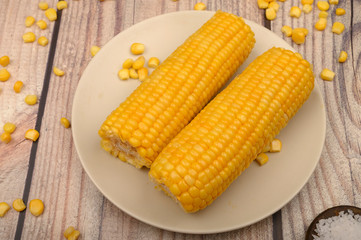 Two ears of boiled corn in a plate, corn kernels and coarse salt on the table. Healthy diet. Fitness diet. For a sweet treat.