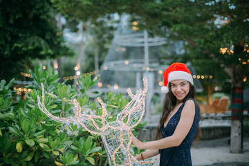 Girl in a Christmas hat next to a decorative deer. New Year in the tropics