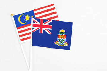 Fototapeta premium Cayman Islands and Malaysia stick flags on white background. High quality fabric, miniature national flag. Peaceful global concept.White floor for copy space.