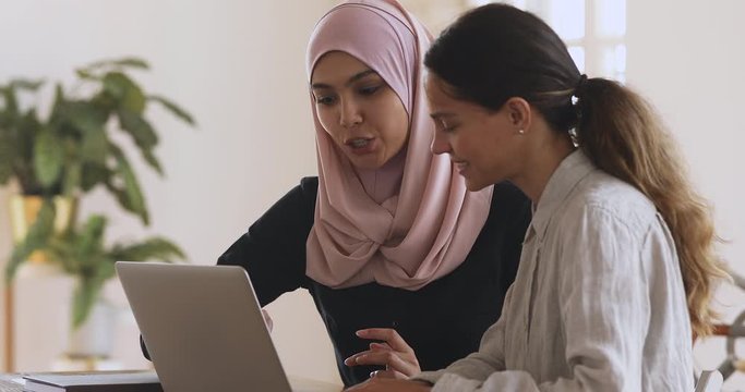 Muslim female mentor helping caucasian intern explaining computer work