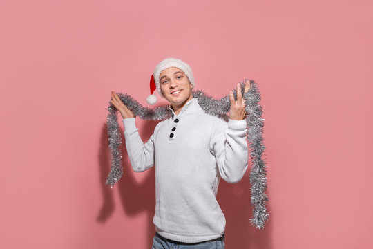 Handsome man in a white sweater, Santa hat and trumpery is happy to celebrate Christmas and New Year.