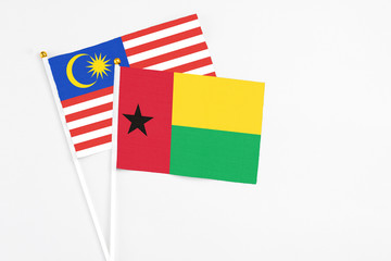 Guinea Bissau and Malaysia stick flags on white background. High quality fabric, miniature national flag. Peaceful global concept.White floor for copy space.