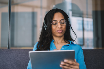 Black woman in headphones with important appearance browsing in tablet