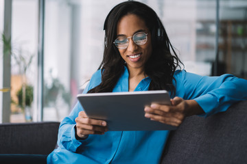 Smiling black brunette woman in headphones having rest with tablet