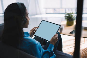 Young black woman surfing tablet while listening to music at home