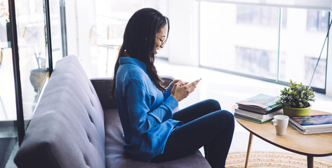 Smiling elegant ethnic lady concentrating on smartphone screen