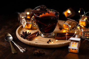 Christmas delicious hot mulled wine with orange, apple, cinnamon, clove, cardamom and anise on wooden plate. Brights lights create festive mood. Dark background