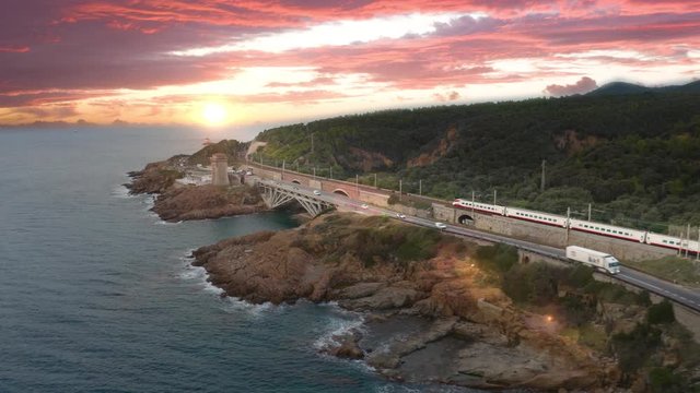 Treno alta velocit&agrave; in transito sugli scogli vicino al mare. Sfondo con cielo al tramonto.