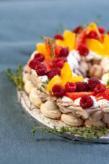 Delicious homemade Pavlova cake decorated with fresh oranges, raspberries and thyme. Traditional french dessert, sweet but light.  Blue background, closeup
