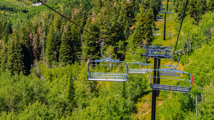 Fototapeta premium Panorama Chairlifts over hiking trails and trees on mountain with buildings in Park City