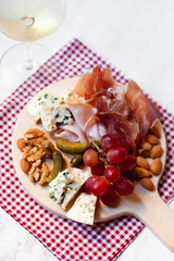 Delicious aperetif for evening home party: wooden borad with french blue cheese, bacon, walnut, almond, italian sweet grapes. Traditional friday apero. Glass of white wine. White background close up