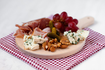 Delicious aperetif for evening home party: wooden borad with french blue cheese, bacon, walnut and almond, italian sweet grapes. Closeup, white background