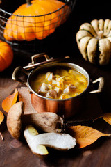 Delicious hot porcini soup in copper pan. Tasty seasonal autumn meal. Fresh mashrooms illustrate ingredients. Concept of homemade food. Closeup, dark wooden background. Pumpkin on the back
