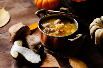 Delicious hot porcini soup in copper pan. Tasty seasonal autumn meal. Fresh mashrooms illustrate ingredients. Concept of homemade food. Closeup, dark wooden background. Pumpkin on the back