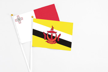 Brunei and Malta stick flags on white background. High quality fabric, miniature national flag. Peaceful global concept.White floor for copy space.