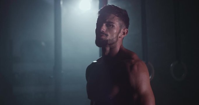 Good looking guy with a perfect body he stretching the head before start a hard workout training in a dark cross fitness class