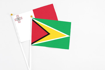 Obraz premium Guyana and Malta stick flags on white background. High quality fabric, miniature national flag. Peaceful global concept.White floor for copy space.