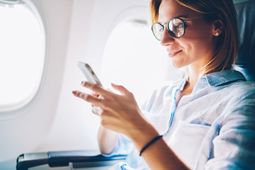 Attractive female passenger of airplane read news from networks via smartphone and wifi on...