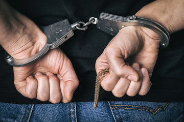 Detained man caught on theft of gold in a store. Handcuffed hands closeup