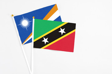 Saint Kitts And Nevis and Marshall Islands stick flags on white background. High quality fabric, miniature national flag. Peaceful global concept.White floor for copy space.