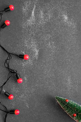 Christmas tree and red garland are on a black background with snow, top view, flat lay.