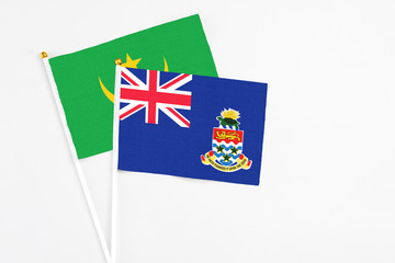 Fototapeta premium Cayman Islands and Mauritania stick flags on white background. High quality fabric, miniature national flag. Peaceful global concept.White floor for copy space.