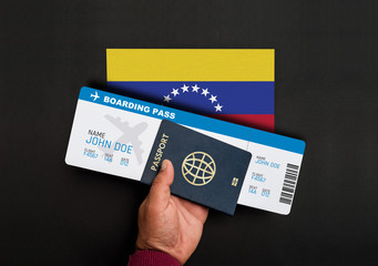 Hand holds passport and boarding pass with flag of Venezuela