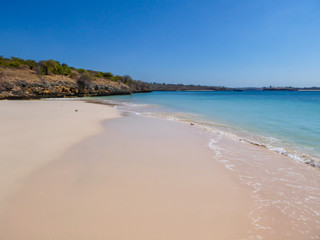 An idyllic Pink Beach on Lombok, Indonesia. Sea is calm, shining with many shades of blue. Beauty in the nature. Unspoiled, hidden gem. In the back there are gentle cliffs overgrown with some bushes