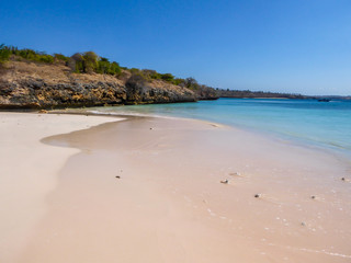 An idyllic Pink Beach on Lombok, Indonesia. Sea is calm, shining with many shades of blue. Beauty in the nature. Unspoiled, hidden gem. In the back there are gentle cliffs overgrown with some bushes
