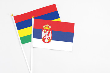 Serbia and Mauritius stick flags on white background. High quality fabric, miniature national flag. Peaceful global concept.White floor for copy space.
