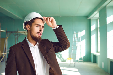 Fototapeta premium Builder foreman in a white helmet surprised in shock at a construction site indoors