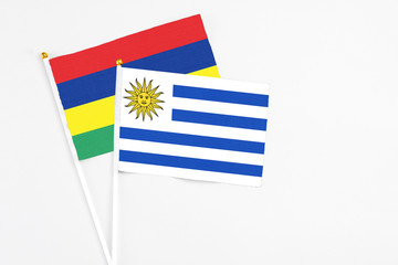 Uruguay and Mauritius stick flags on white background. High quality fabric, miniature national flag. Peaceful global concept.White floor for copy space.