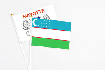 Uzbekistan and Mayotte stick flags on white background. High quality fabric, miniature national flag. Peaceful global concept.White floor for copy space.